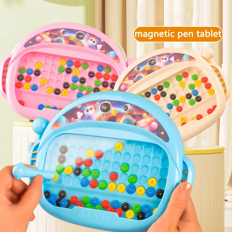 A hand holds a blue magnetic pen tablet with colorful plastic balls, demonstrating the educational art toy.