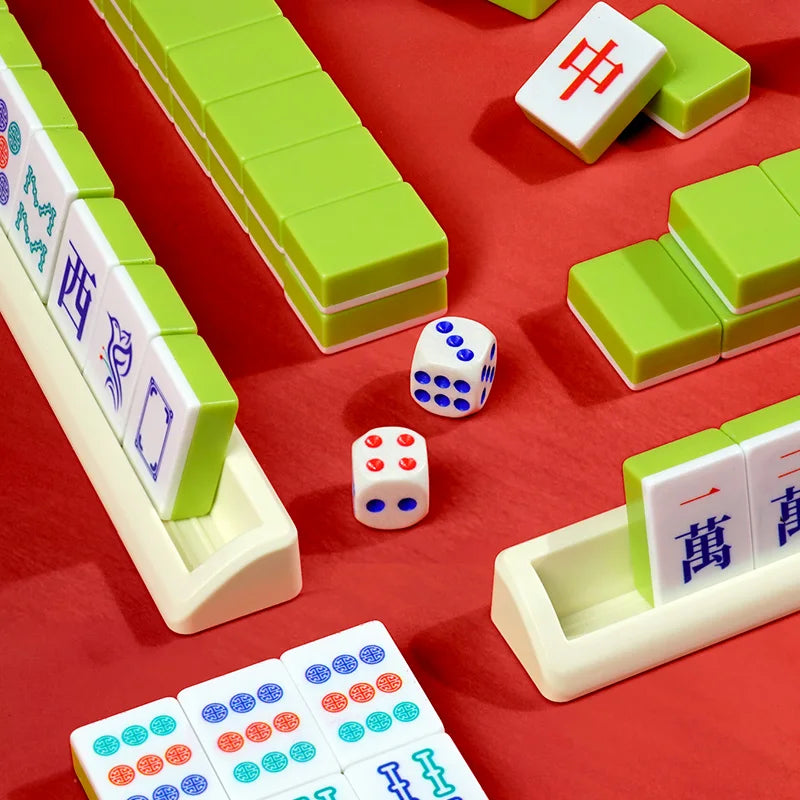 A set of mahjong tiles and dice displayed on a red surface, including green tiles, white tiles, and a carrying case.