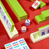 A set of mahjong tiles and dice displayed on a red surface, including green tiles, white tiles, and a carrying case.