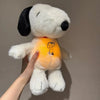 A white plush toy resembling Snoopy with a black ear, being held by a hand.