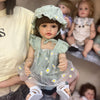 A realistic silicone vinyl toddler doll named Betty with dark hair and a light green dress and bonnet.