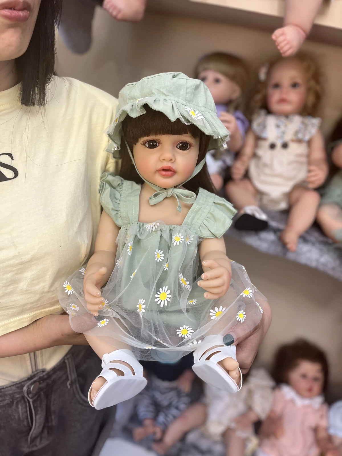 A realistic silicone vinyl toddler doll named Betty with dark hair and a light green dress and bonnet.
