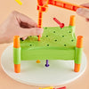A hand is using an orange toddler hammer nails toy to insert colored wooden pegs into a green board.