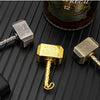 Three hammer-shaped metal fidget spinners with gold and silver finishes displayed on a dark surface.