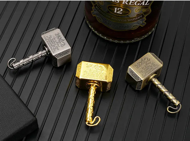 Three hammer-shaped metal fidget spinners with gold and silver finishes displayed on a dark surface.