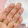 A hand displays a set of three pink resin flower ornaments on the fingers.