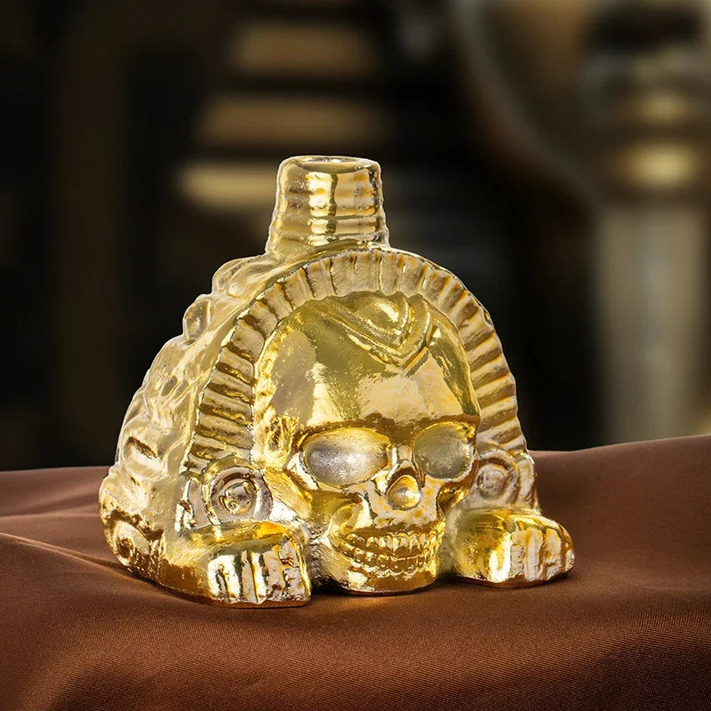 A handcrafted golden Aztec death whistle featuring a skull design resting on brown fabric.