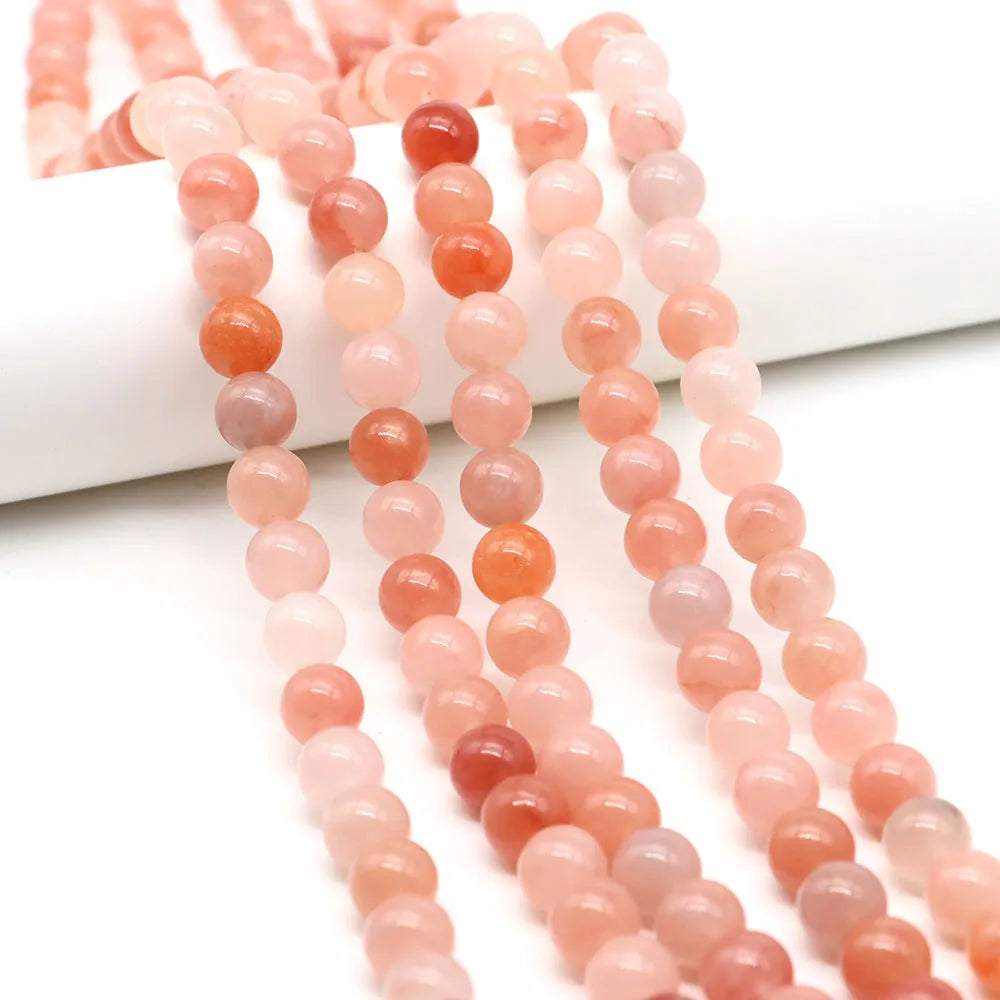 A string of round rose quartz beads in shades of pink and coral, laid out on a white surface.