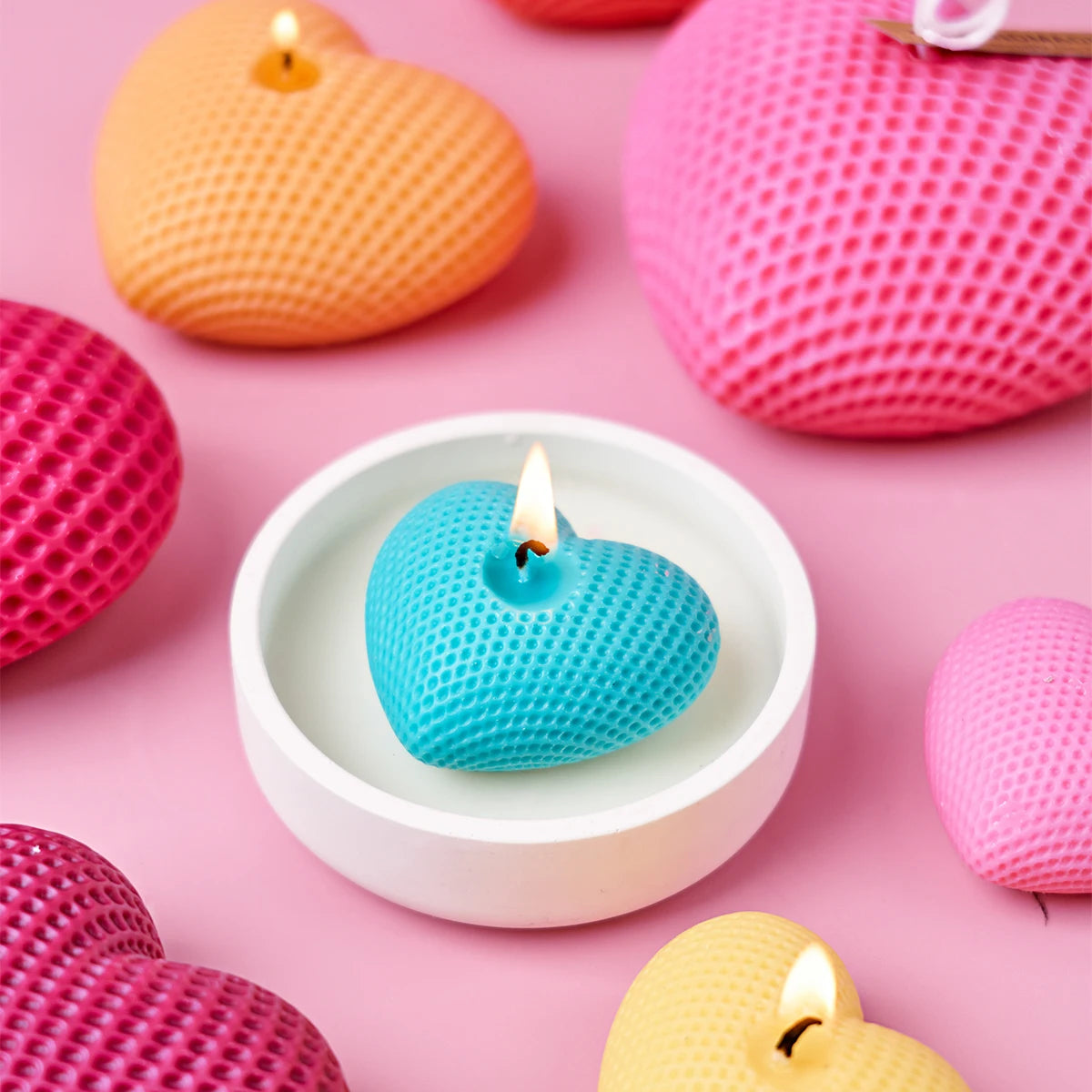 A collection of pink and orange silicone heart-shaped candles and molds on a pink background.