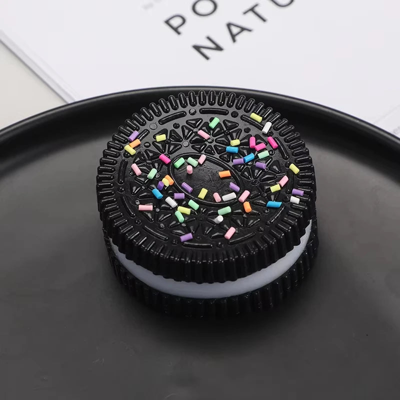 A black biscuit squishy stress relief toy with colorful sprinkles resting on a dark plate.