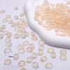 A pile of translucent, pale yellow gradient tulip glass beads is shown next to a white ceramic dish.