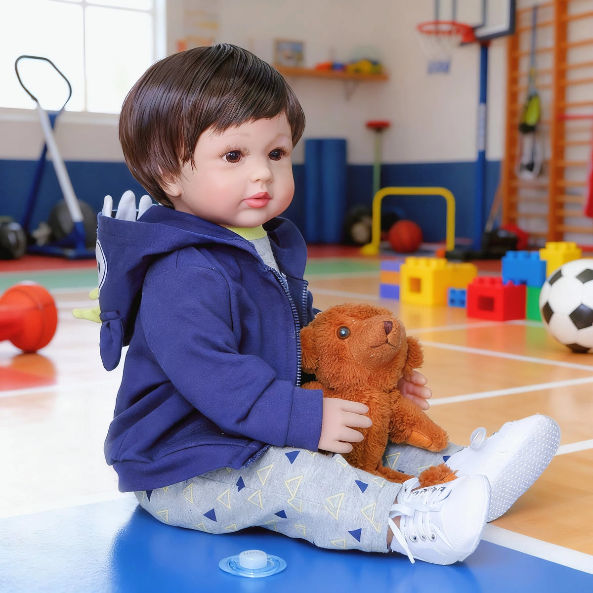 A baby doll with soft cloth body wearing a blue hoodie sitting on a blue surface.