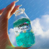 A hand holds a clear glass bottle filled with bright blue liquid, used as a drink cup toy.