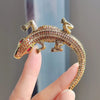 A gold-toned rhinestone turtle brooch pin is held by a hand against a light blue background.