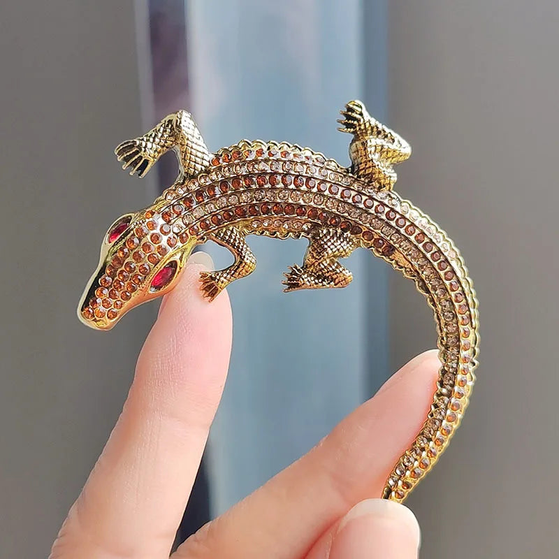 A gold-toned rhinestone turtle brooch pin is held by a hand against a light blue background.