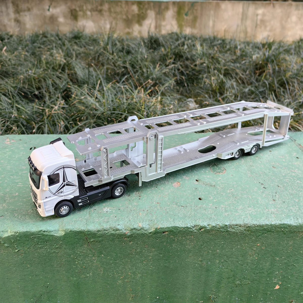 A silver diecast model of a 1:50 scale container truck with lights and sounds on a green surface.