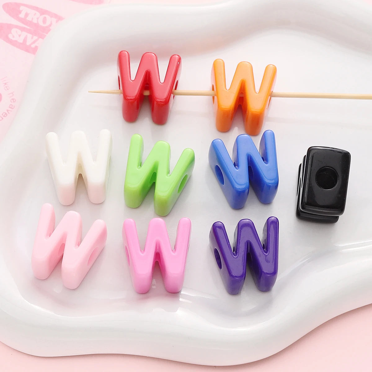 A collection of colorful acrylic letter beads shaped like the letter W in various shades and colors arranged on a white tray.