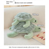 A soft, light green sea turtle plush toy is shown lying on a white surface.