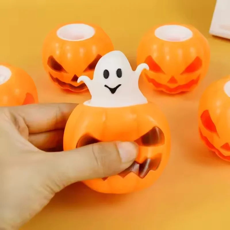 A hand holds an orange squishy ghost shaped like a pumpkin, with other similar toys in the background.