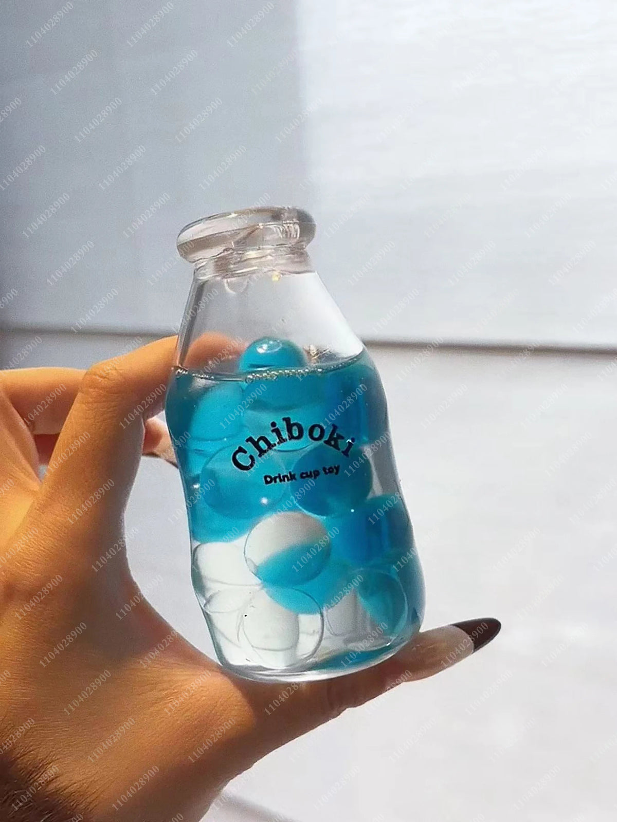 A hand holds a clear glass bottle filled with blue liquid and white squishy balls labeled Chiboki.