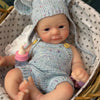 A hand-painted silicone reborn doll wearing a knitted elf hat and outfit, resting in a woven basket.
