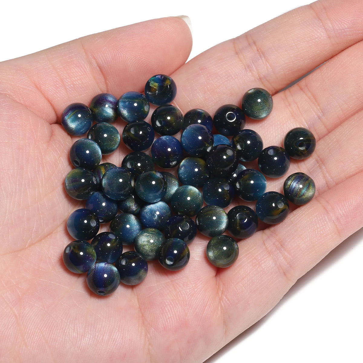 A hand holds a cluster of dark blue and green tiger eye resin beads for jewelry making.
