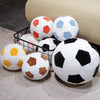A collection of realistic football plush pillows in various colors including white, orange, blue, and black resting on a ligh