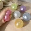 A hand holds a variety of translucent, spherical fidget balls in shades of green, purple, white, and yellow on a wooden surfa