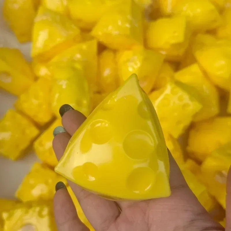 A hand holds a yellow, triangular squeeze toy shaped like a cheese ball stress relief item.