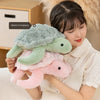 A woman is holding a soft, pink sea turtle plush toy next to her face in a warm, cozy setting.
