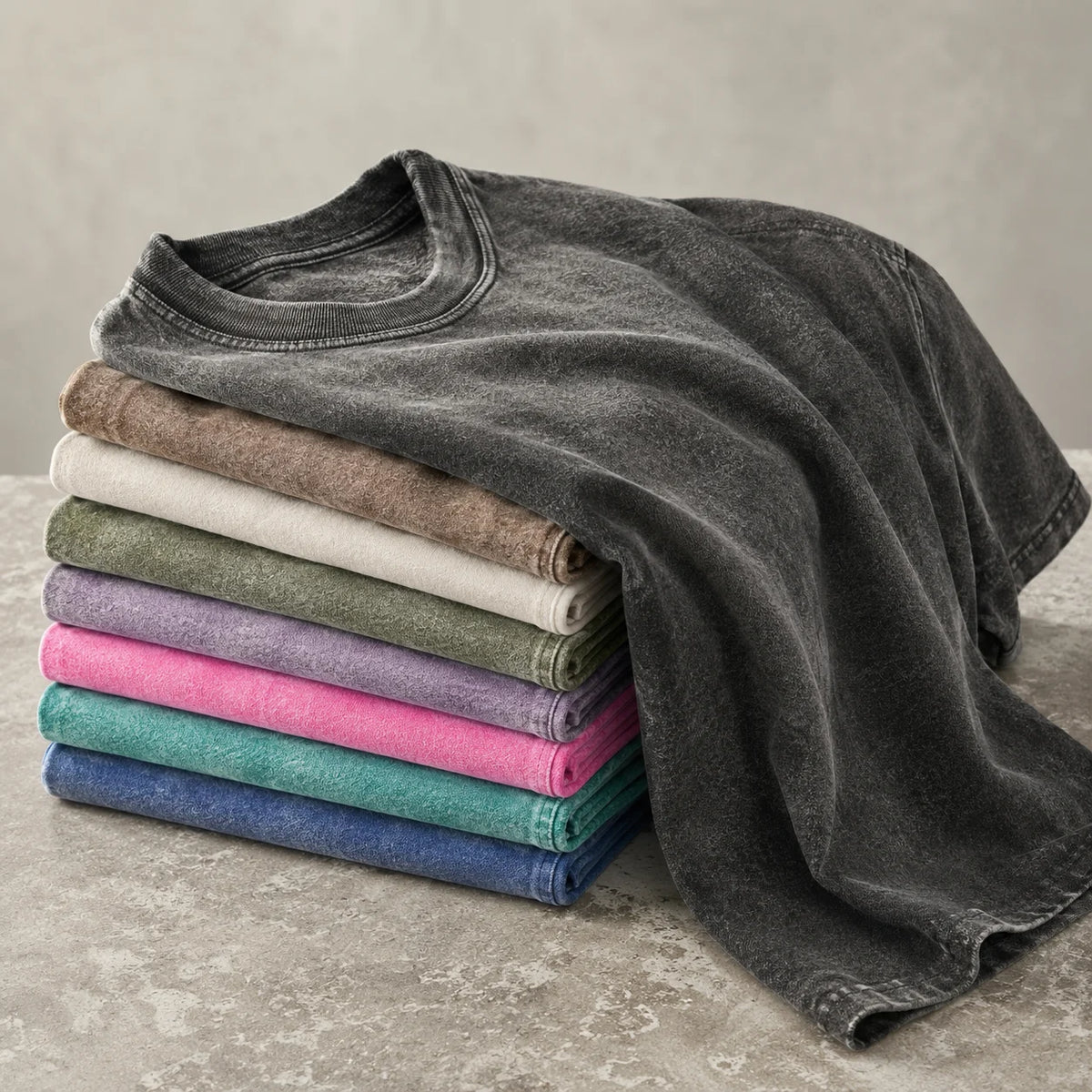 A stack of gray and colored oversized t-shirts, including heather gray, beige, olive green, and pink.