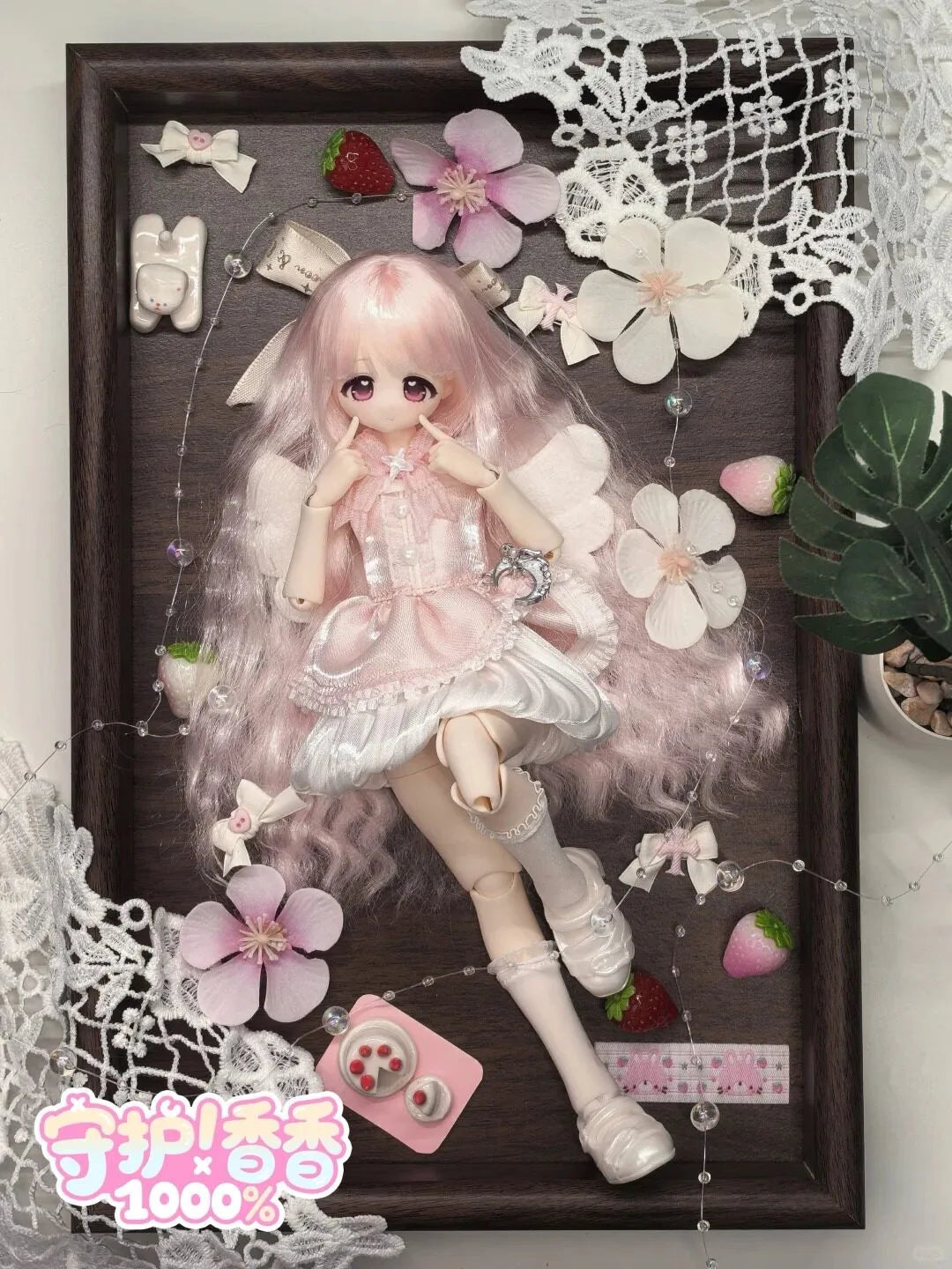A detailed figure of a pink-haired girl in a frilly dress with white accents, displayed in a wooden frame surrounded by lace 