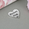 A silver heart-shaped keychain token engraved with the words Pocket Hug.