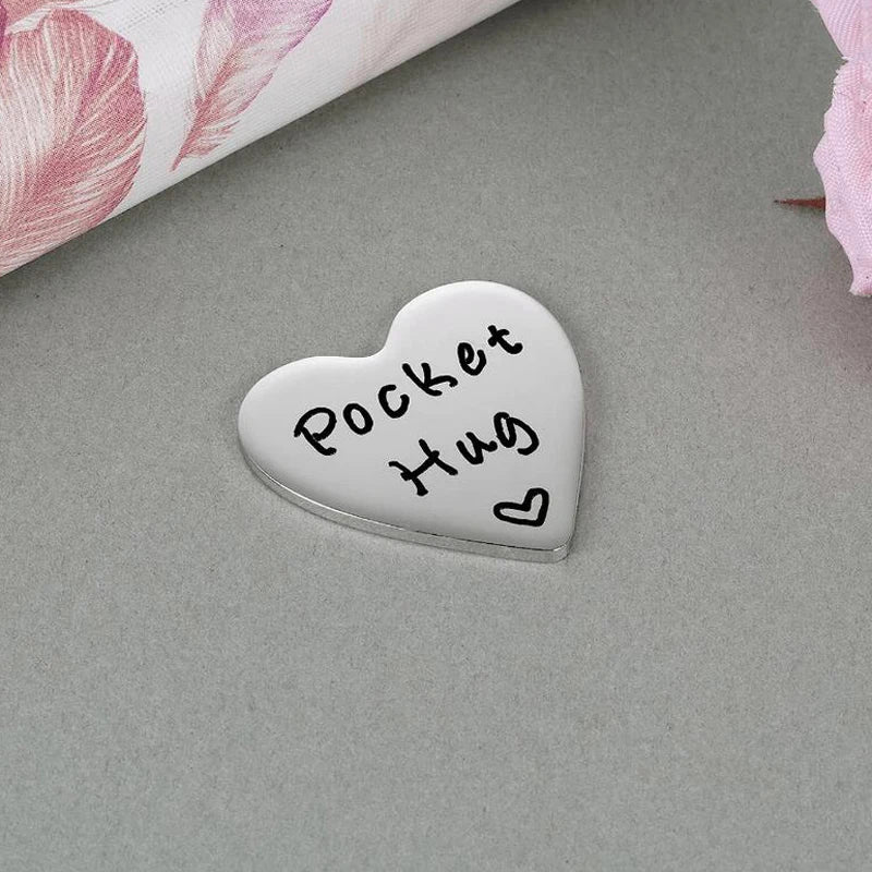A silver heart-shaped token engraved with the words Pocket Hug Hug for a long distance keepsake gift.
