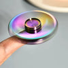 A colorful metal fidget spinner with a polished finish is held above a gray surface.