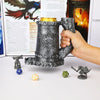 A hand holds a dark gray metal dice tower mug featuring a wolf emblem, with several dice and a small figurine nearby.