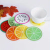 A set of colorful fruit pattern PVC coasters, including watermelon, kiwi, orange, and lime designs, displayed next to a white