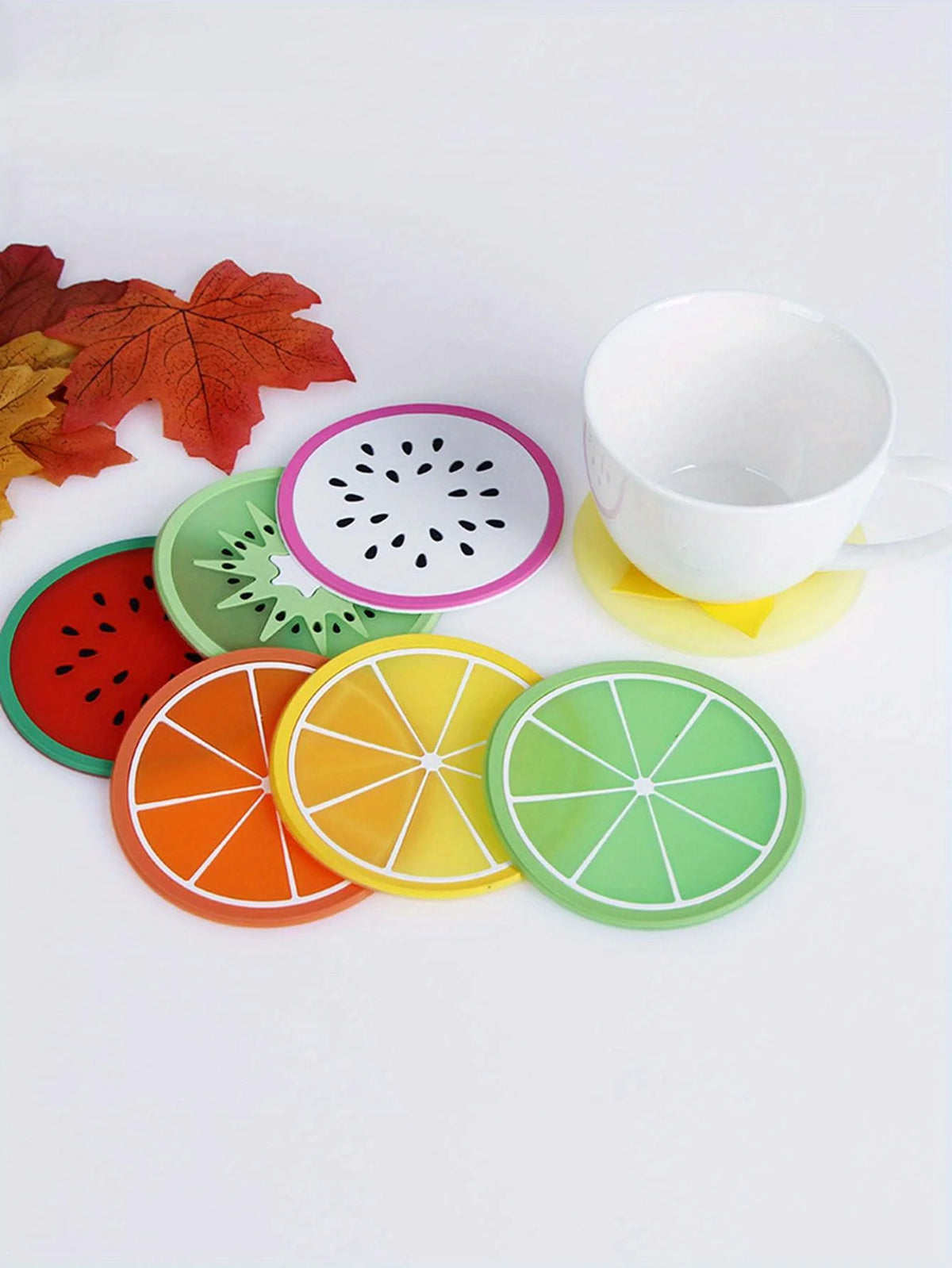 A set of colorful fruit pattern PVC coasters, including watermelon, kiwi, orange, and lime designs, displayed next to a white