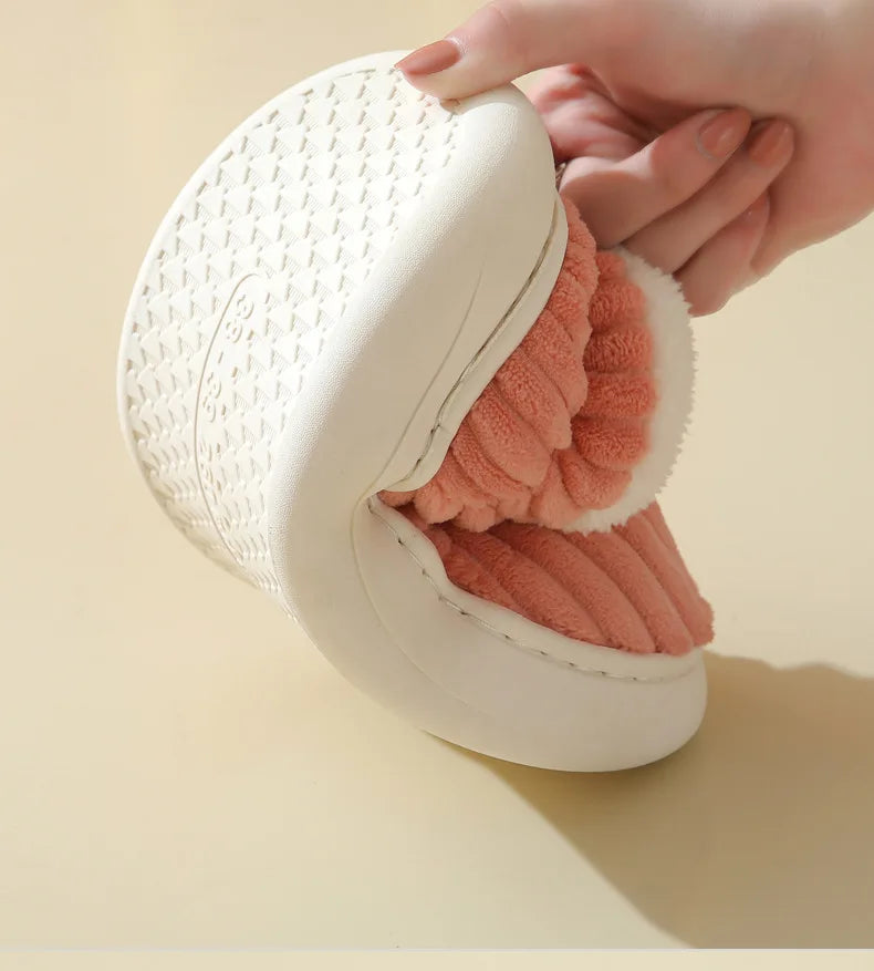 A hand is holding a white faux fur slipper with a pink interior lining.