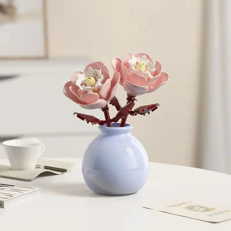 A small vase holds a pink floral bouquet made of building blocks on a white table.