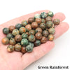 A handful of natural stone round beads in various shades of green and brown, used for jewelry making.