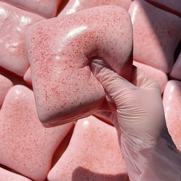 A hand wearing a clear glove squeezes a pink, speckled toast-shaped fidget toy.