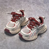 A pair of red and white breathable mesh kids running sneakers with cushioned soles resting on a gray surface.