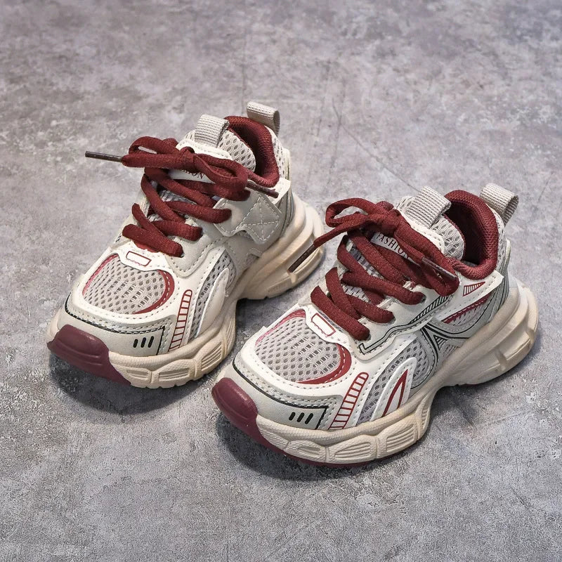 A pair of red and white breathable mesh kids running sneakers with cushioned soles resting on a gray surface.