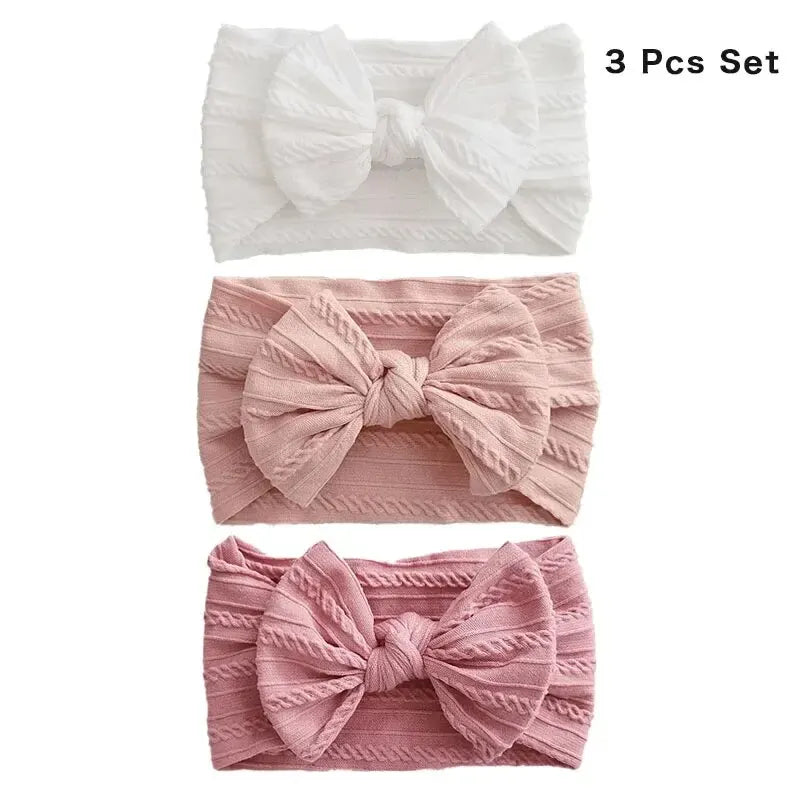 A set of three soft stretch baby headbands with bows in white and pink shades.