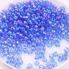 A pile of small, iridescent blue and purple glass rice beads for DIY jewelry and crafting.