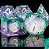 A collection of iridescent liquid core dice in purple and teal colors, including a large green die and smaller dice.