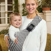 A smiling woman is wearing an adjustable baby sling carrier with a patterned fabric while holding a happy baby.