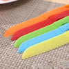 A set of five colorful plastic safety knives in orange, red, green, blue, and yellow laid diagonally on a woven mat.