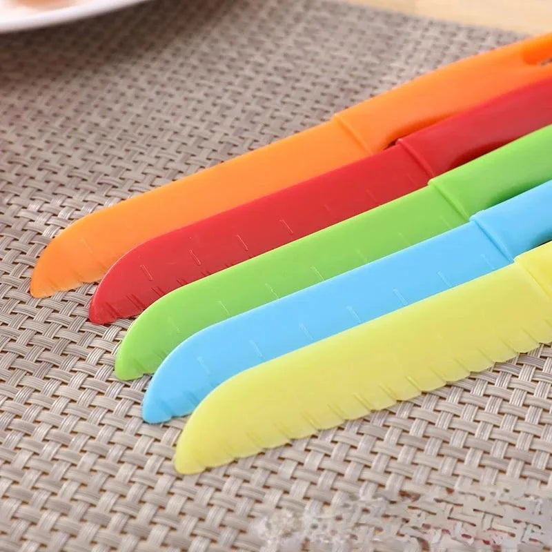 A set of five colorful plastic safety knives in orange, red, green, blue, and yellow laid diagonally on a woven mat.